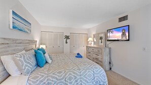 A bedroom with a bed, a dresser, a TV, and a closet. - White Sands On Siesta 1 Bedroom Condo (Siesta Key)