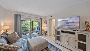 A living room with a sofa, TV, and a balcony with a view of the sea. - White Sands On Siesta 1 Bedroom Condo (Siesta Key)