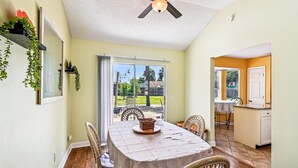 A dining area with a table, chairs, and a ceiling fan. There is a sliding glass door leading to a patio with outdoor furniture. - 17007 Firenzo Ave 3 Bedroom Home (Panama City Beach)