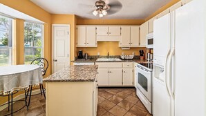 A compact kitchen with white cabinets, a granite countertop, a built-in oven, and a refrigerator. - 17007 Firenzo Ave 3 Bedroom Home (Panama City Beach)