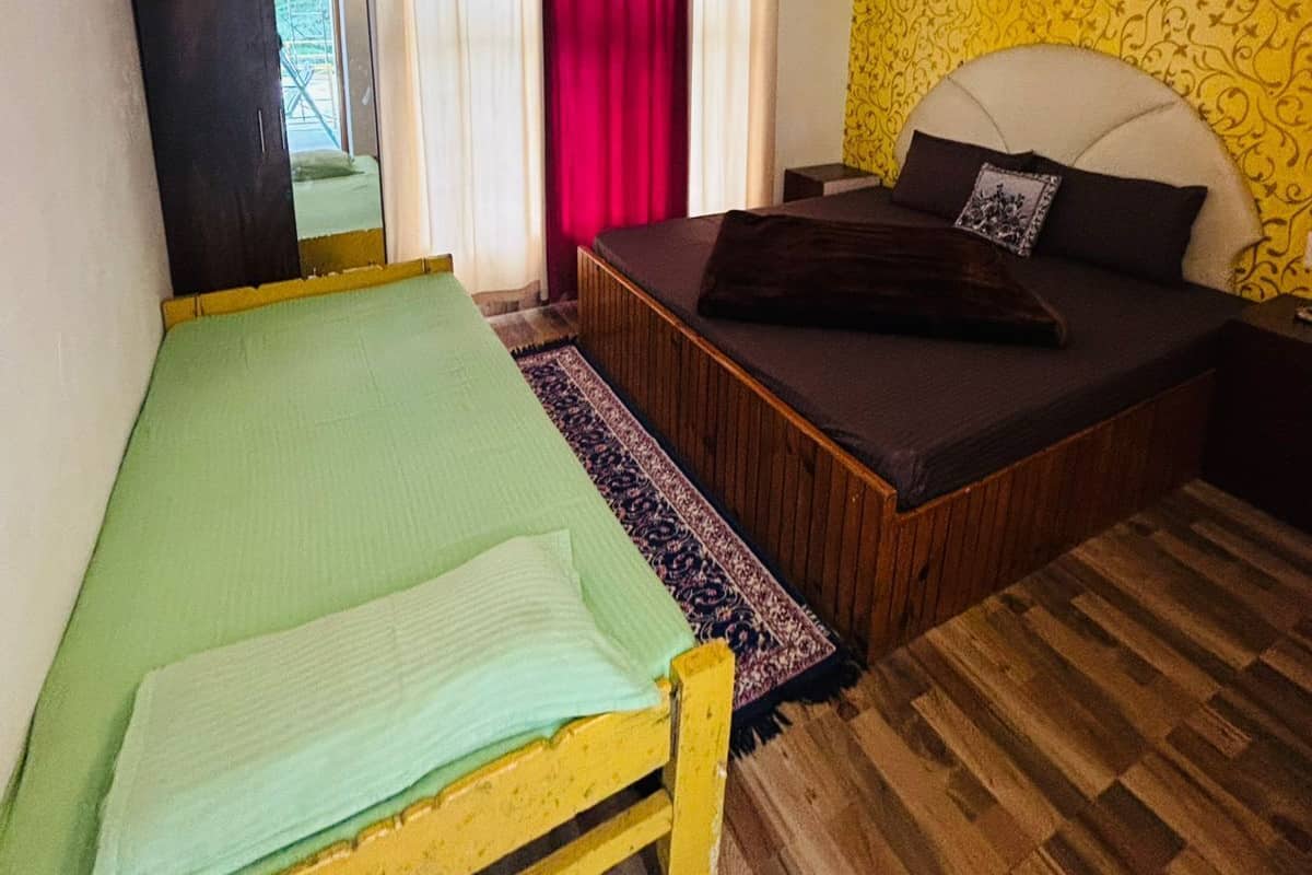 Una habitación con cama, sofá cama, piso de madera, espejo y ventana con cortinas.