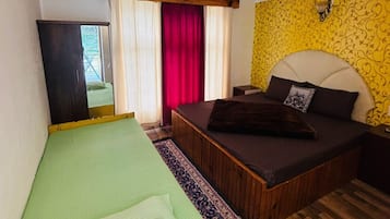 A room with a bed, a sofa bed, a wooden floor, a mirror, and a window with curtains.
