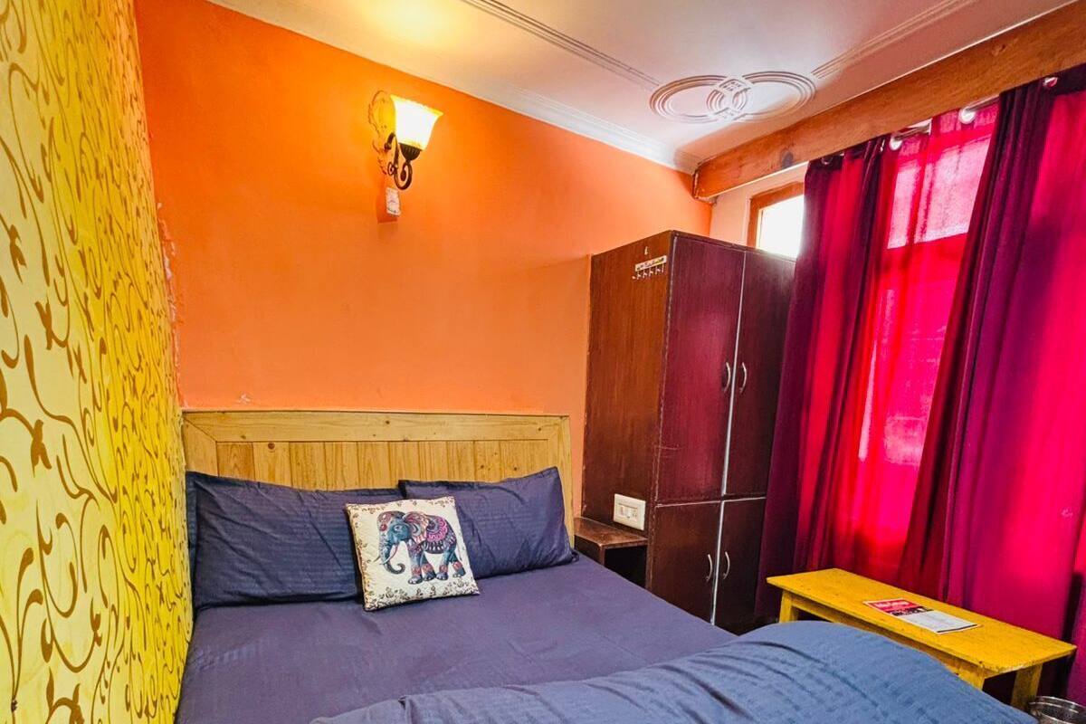 Un dormitorio con cama, cabecera de madera, mesita de noche, armario y ventana con cortinas rojas.