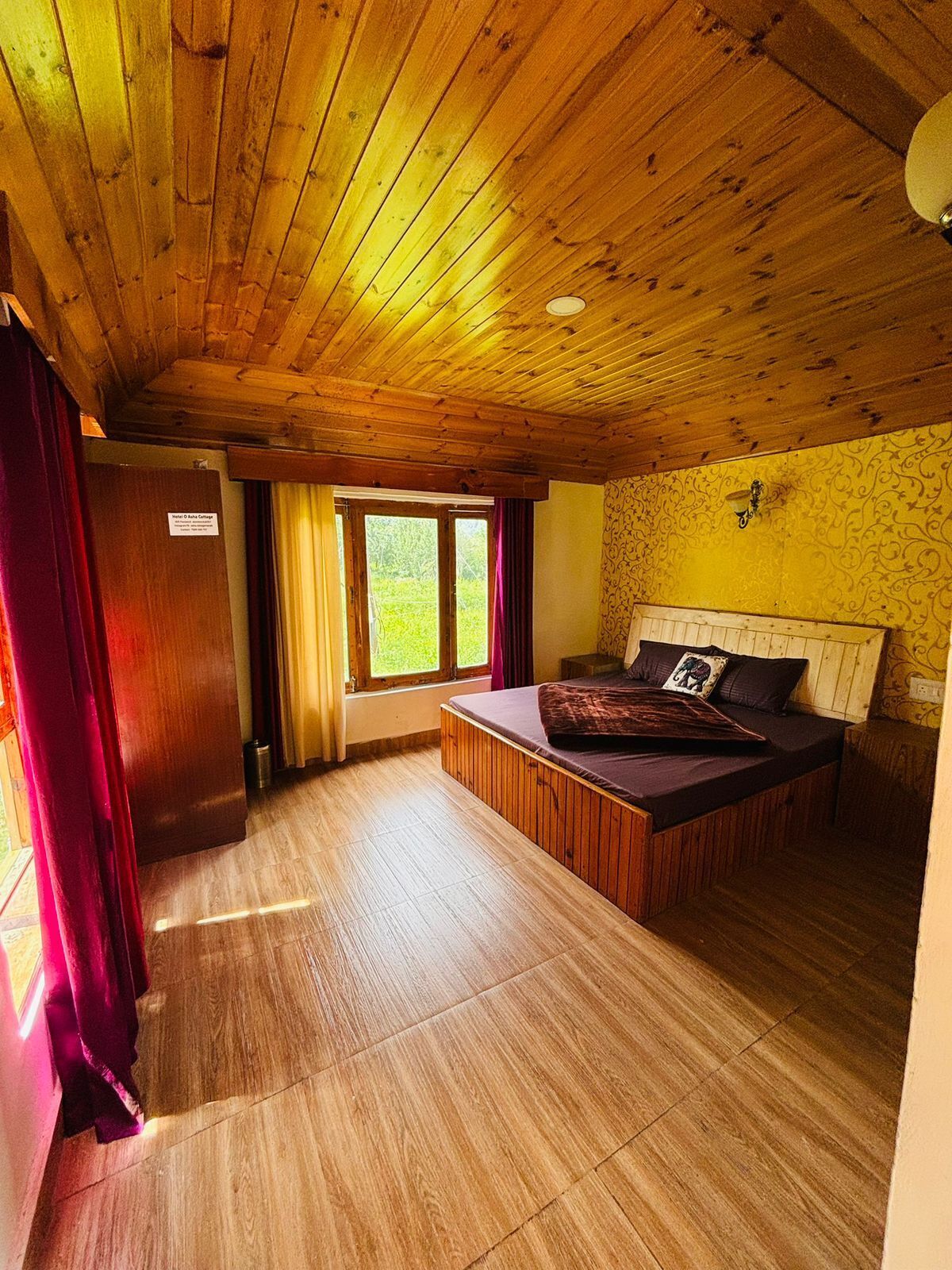 A wooden-paneled room with a bed, a window with curtains, and a door.