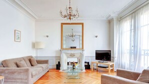 A spacious living room with a fireplace, a sofa, a television, and a chandelier.
