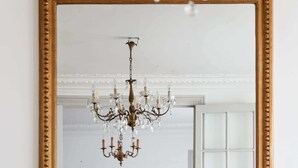 A room with a large ornate mirror, a chandelier, and a fireplace.