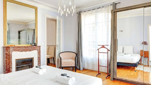 A hotel room with a large bed, a mirror, a fireplace, a chair, and a wardrobe with a mirror.