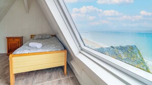 A bedroom with a bed, a nightstand, and a view of the beach and ocean through a window.
