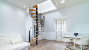 A modern living room with a spiral staircase, a white sofa, and a dining area with white chairs.