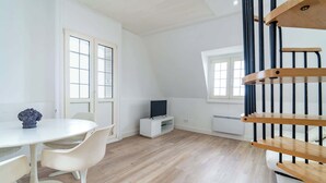 A modern, well-lit room with a white table, chairs, a TV on a white stand, and a wooden staircase.