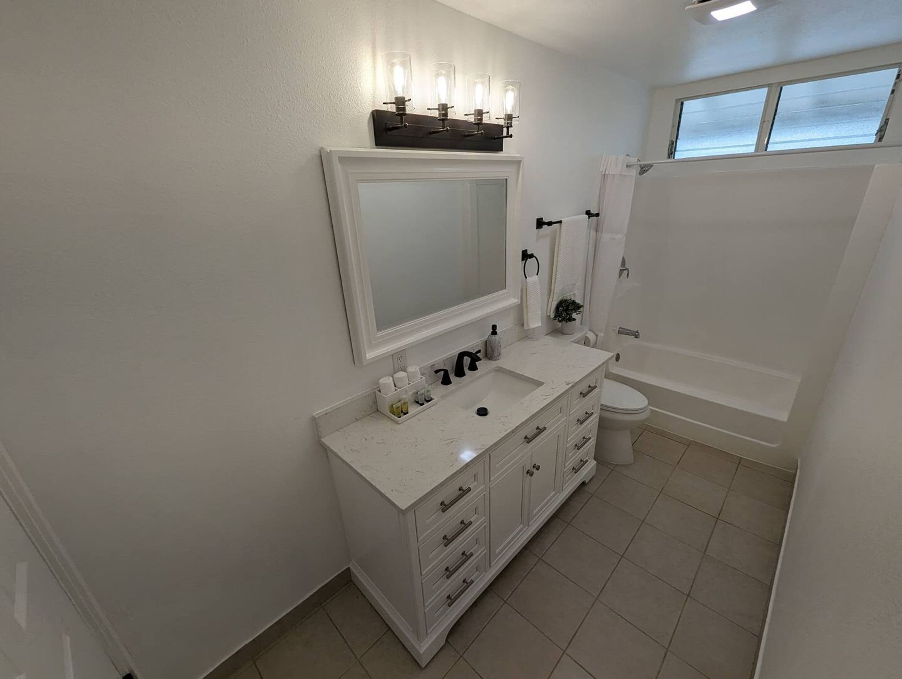 A modern bathroom with a white vanity, a large mirror, a toilet, and a bathtub.