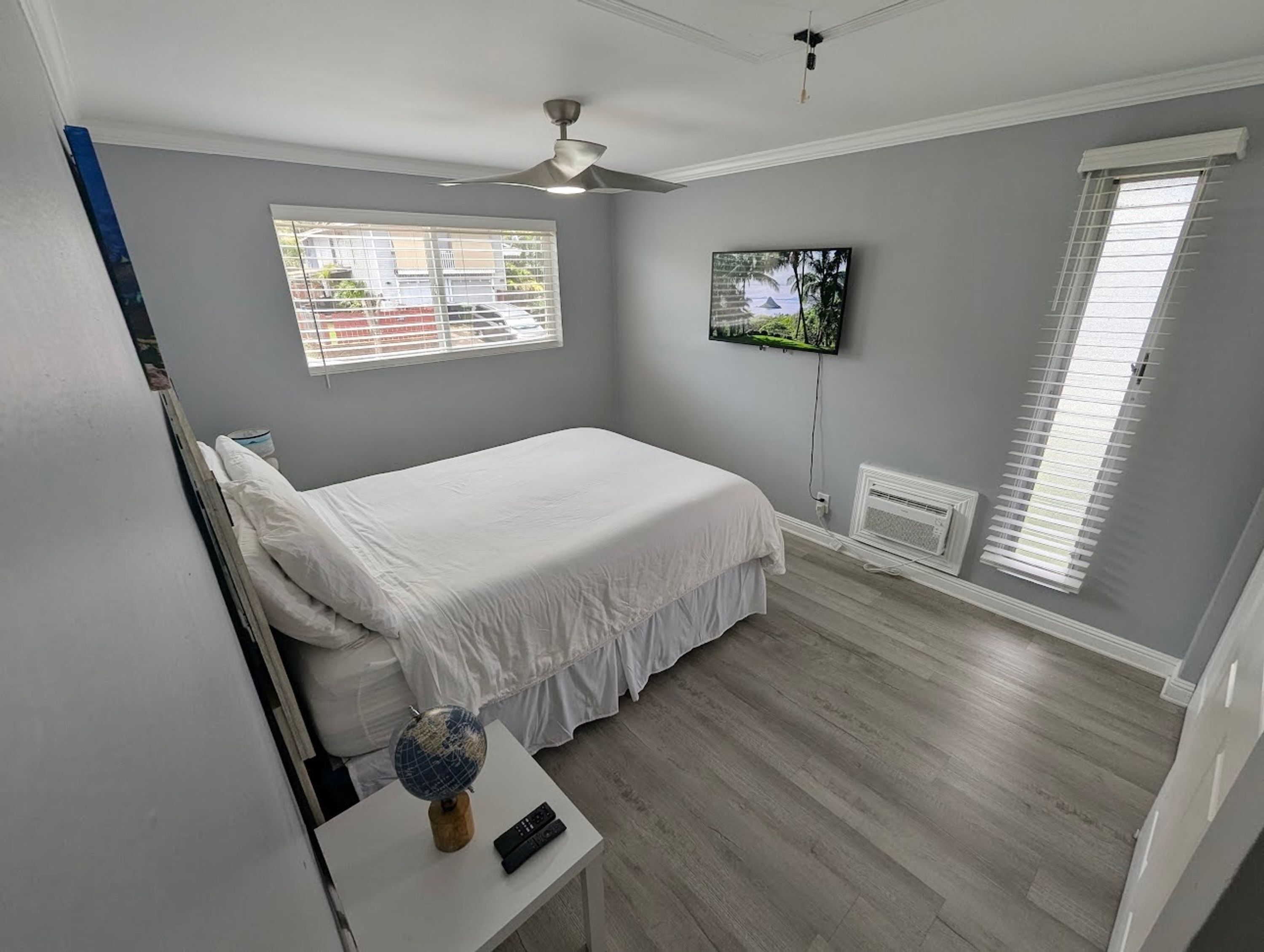 A bedroom with a bed, a globe on a nightstand, a TV on the wall, and windows with blinds.