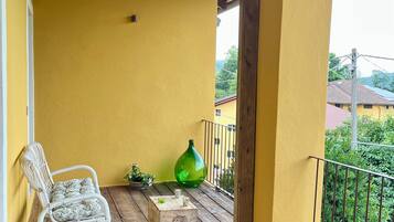 A wooden deck with a yellow wall, a wicker chair, a green vase, and a welcome mat.