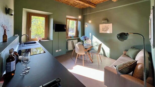 Une cuisine moderne dotée d’une cave à vin intégrée, un coin repas avec une table et des chaises, et un espace de vie chaleureux avec un canapé et une lampe.