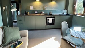 Une cuisine moderne dotée d’un four encastré, un coin repas avec une table en verre et un espace salon confortable avec un canapé.