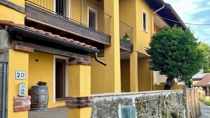 Un bâtiment jaune avec un balcon, un mur en pierre et un arbre.