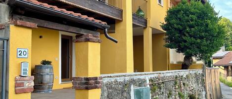 A yellow building with a balcony, a stone wall, and a tree.
