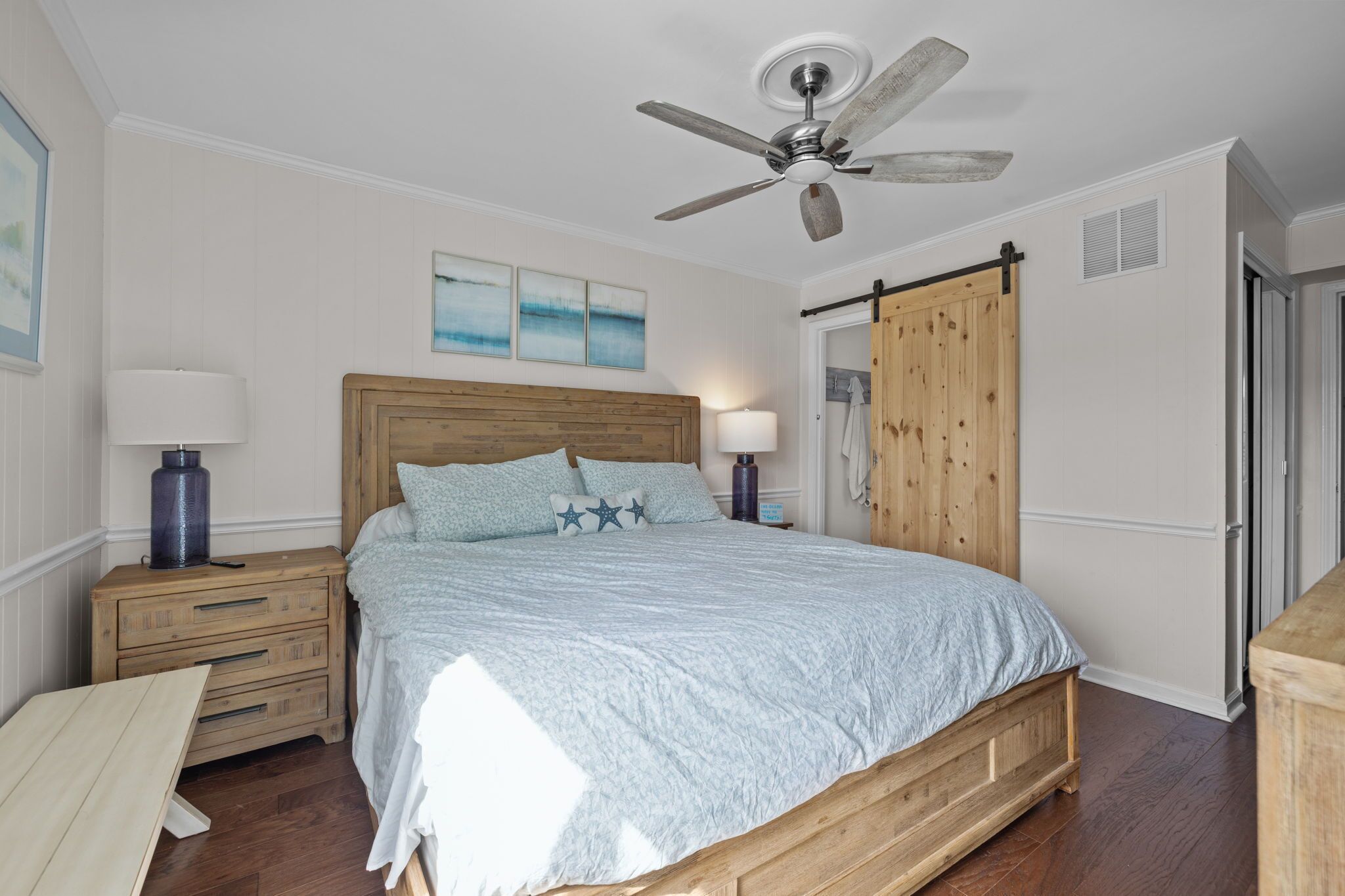 A bedroom with a wooden bed, two bedside tables with lamps, a ceiling fan, and a wooden wardrobe.