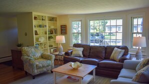 A living room with a brown leather sofa, a floral armchair, a wooden coffee table, and a bookshelf. - 3 Bedroom home in West Harwich, sleeping 6 (West Harwich)