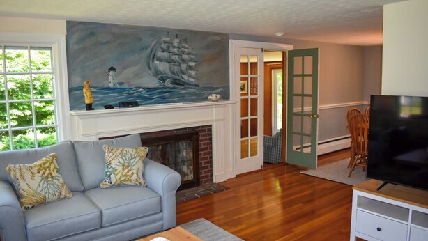 A living room with a fireplace, a sofa, a television, and a painting of a ship and lighthouse. - 3 Bedroom home in West Harwich, sleeping 6 (West Harwich)