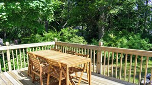 A wooden deck with a table and chairs, surrounded by a wooden railing and lush greenery. - 3 Bedroom home in West Harwich, sleeping 6 (West Harwich)