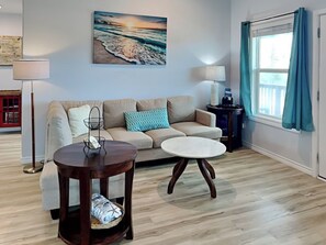 A living room with a beige sofa, a round coffee table, and a painting of a beach scene.