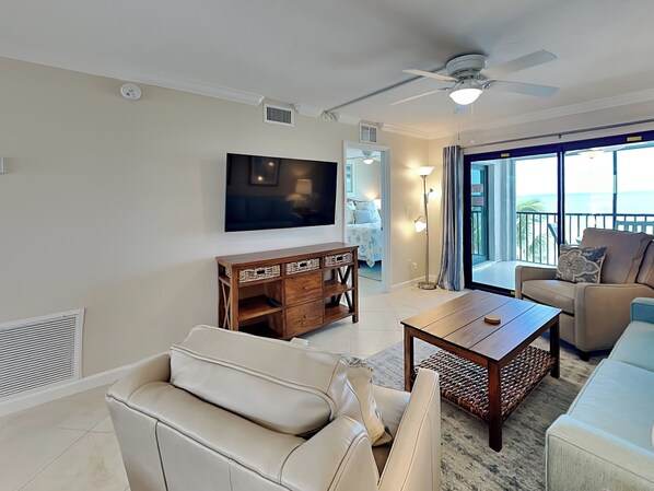 A modern living room with a flat-screen TV, a ceiling fan, a wooden coffee table, and a sofa. - Seaside 404 | Breathtaking Views + Resort Perks (Fort Myers Beach)
