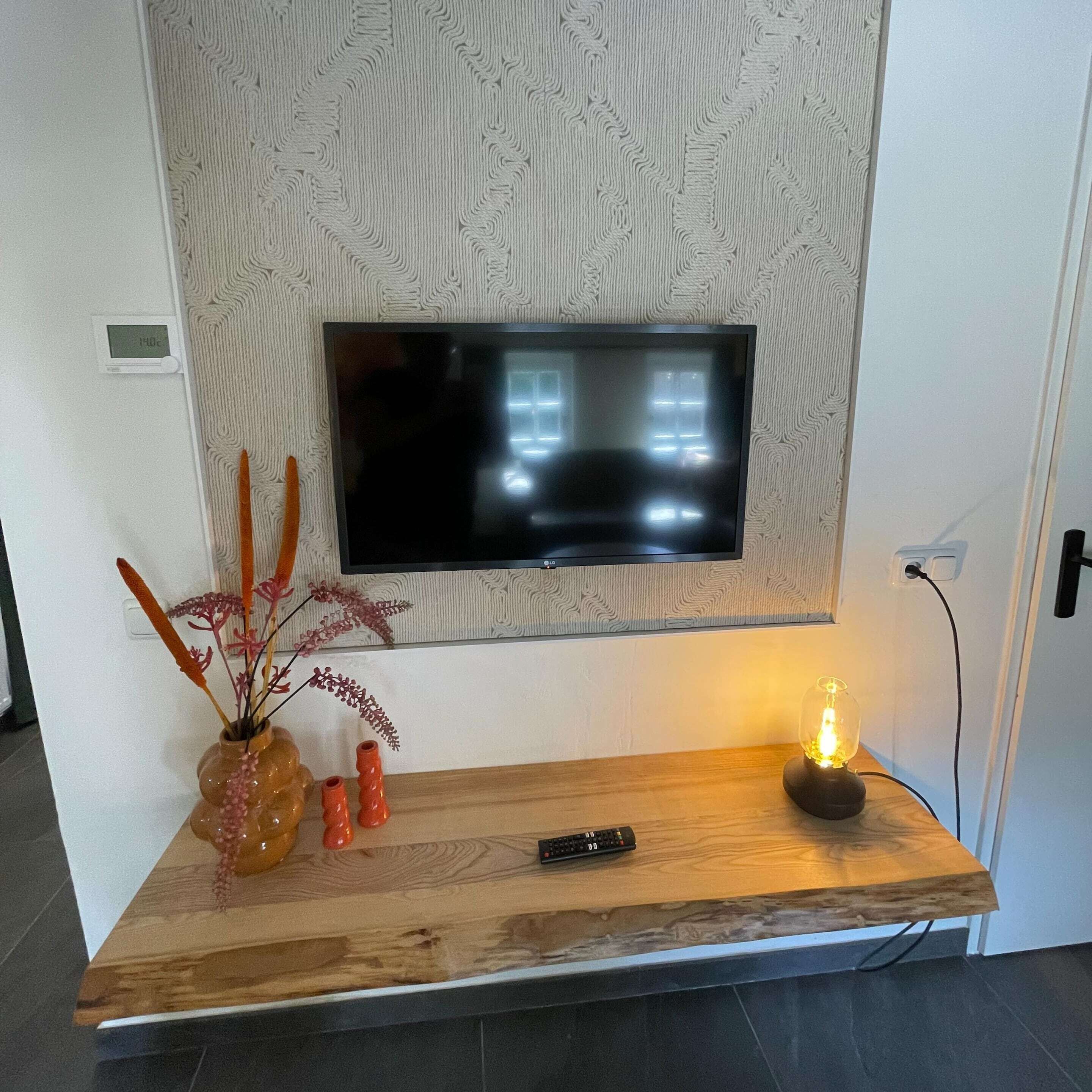 Una sala de estar moderna con un televisor de pantalla plana montado en una pared texturizada, un mueble bajo de madera con objetos decorativos y un control remoto.