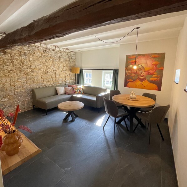 Una sala de estar acogedora con una pared de piedra, un sofá, una mesa de comedor con sillas y un cuadro en la pared.