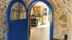 Una puerta azul da paso a una habitación con paredes de piedra y se puede ver una cocina al otro lado.