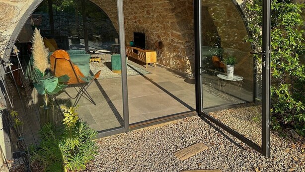 Un patio moderno al aire libre con un muro de piedra de fondo, muebles para sentarse y un cerramiento de cristal.
