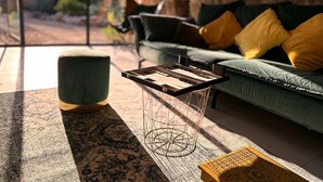 Una sala de estar acogedora con pared de piedra, un sofá verde con cojines amarillos, una mesa de centro de madera y un taburete azul.