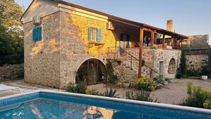 Una casa de piedra con piscina, ventanas de arco y un espacio al aire libre cubierto.