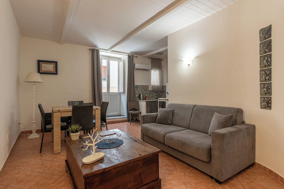 A living room with a grey sofa, wooden coffee table, and a dining area with a table and chairs.