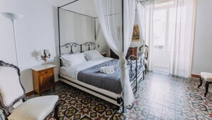 A four-poster bed with a canopy, a bedside table with a lamp, a chair, and a patterned floor. - Real Umberto Apartments by Wonderful Italy (Palermo)