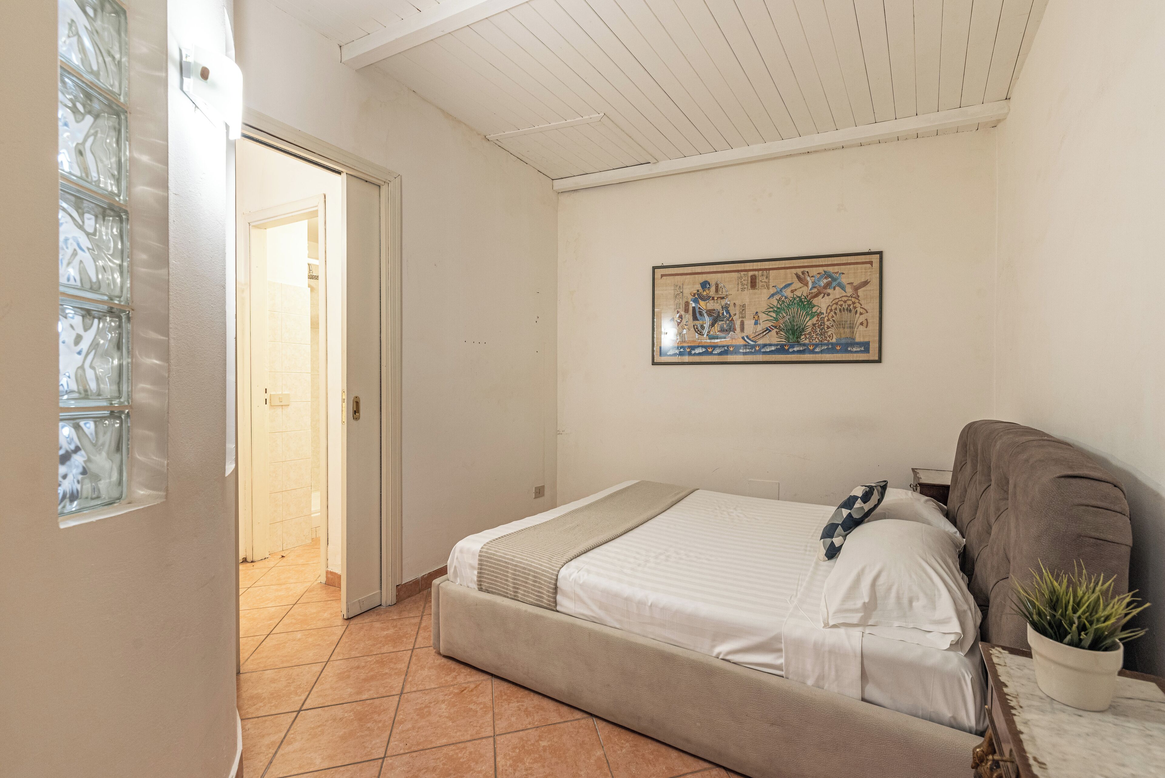 Een slaapkamer met een bed, een potplant en een schilderij aan de muur.