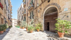 A cobblestone street lined with potted plants and historic buildings with arched doorways. - Real Umberto Apartments by Wonderful Italy (Palermo)