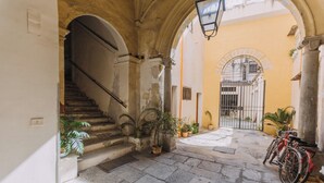 A narrow stone-paved courtyard with a staircase leading to an upper level, potted plants, and a bicycle parked against a wall. - Real Umberto Apartments by Wonderful Italy (Palermo)