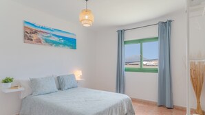 Un dormitorio con cama, un cuadro, una lámpara colgante, ventana con cortinas y vista al paisaje.