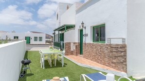 Un edificio blanco con una puerta verde, un patio con mesa y sillas, y una parrilla.