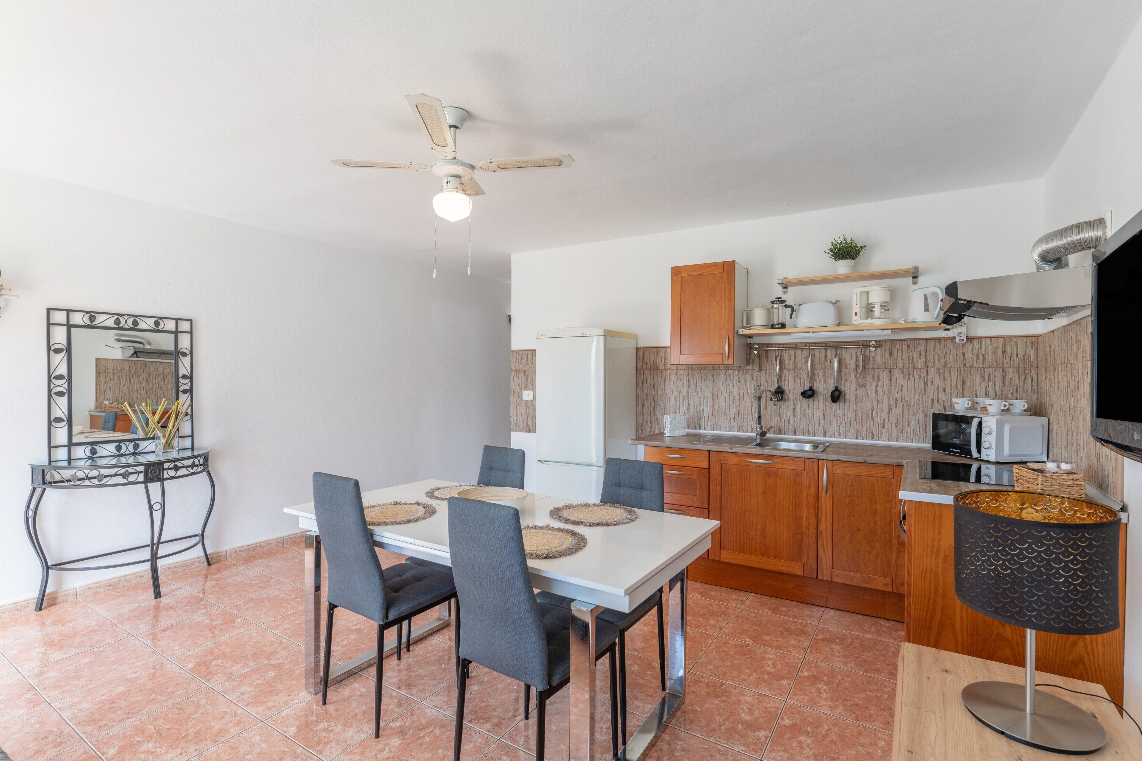 Una cocina moderna con armarios de madera, un refrigerador blanco y una zona de comedor con una mesa y sillas blancas.
