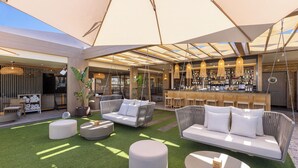 An outdoor seating area with a bar, cushioned seating, and a green artificial turf floor. - Maspalomas Villas by Dunas - Only Adults (San Bartolome de Tirajana)
