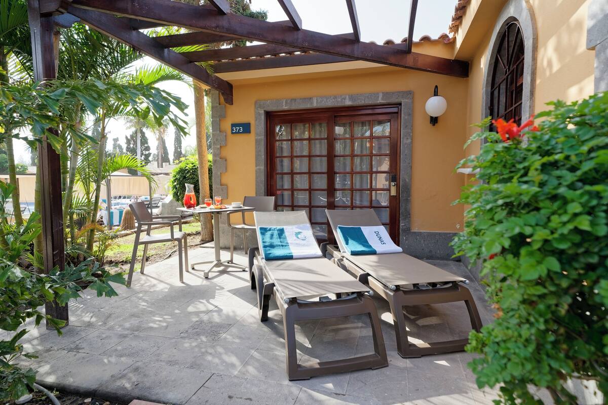 A covered outdoor seating area with two lounge chairs, a table, and a chair.