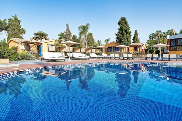 Une piscine entourée de palmiers et d’immeubles, avec des chaises longues et des parasols.