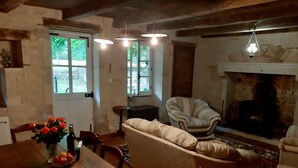 A rustic living room with a sofa, a fireplace, and a dining area with a table and chairs. - Charming cottage with all the comforts of home in Les Adjots (Les Adjots)