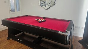 Ein Billardtisch mit roter Spielbahn, ein Satz Billardkugeln und ein dekorativer Spiegel an der Wand.
