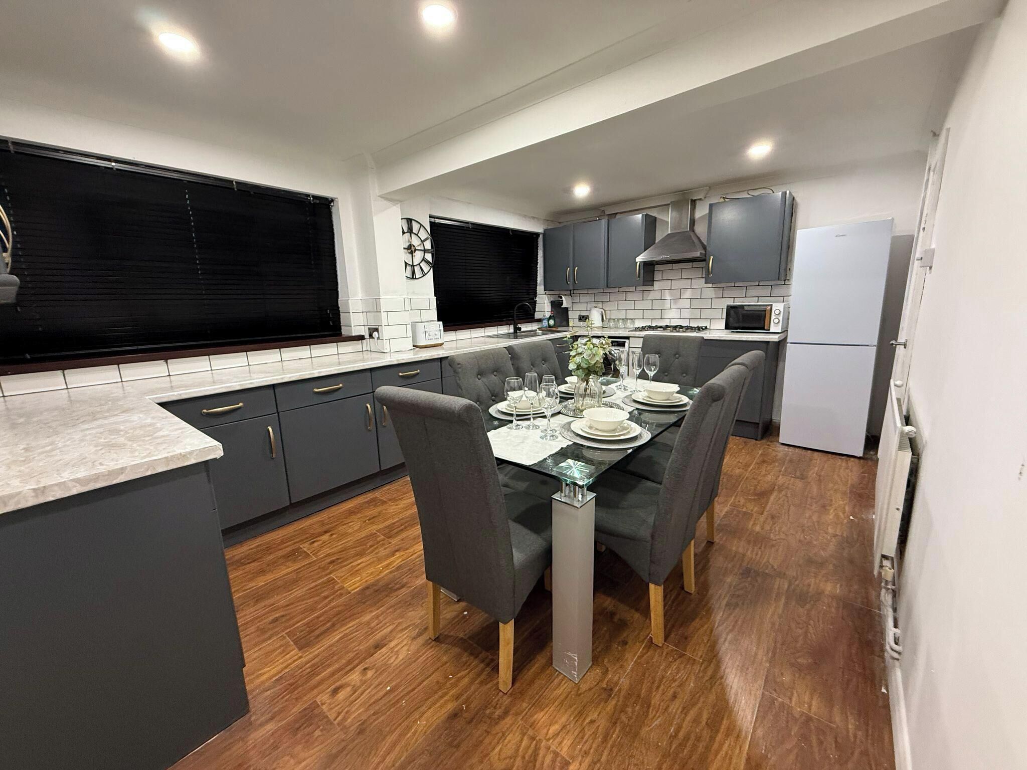 A modern kitchen with grey cabinets, a dining table set for four, and a large window with blinds.