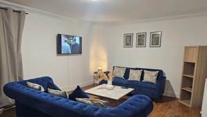 Ein Wohnzimmer mit zwei blauen Sofas, einem Couchtisch und einem an der Wand montierten Fernseher.