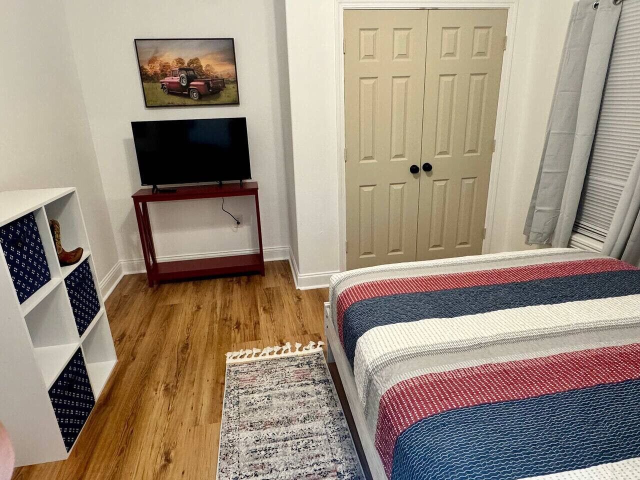 Een slaapkamer met een bed, een televisie op een standaard, een deur en een plank met dozen met een patroon.