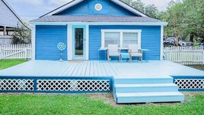 Une maison bleue avec un porche à l’avant, une petite terrasse et une clôture blanche en bois.